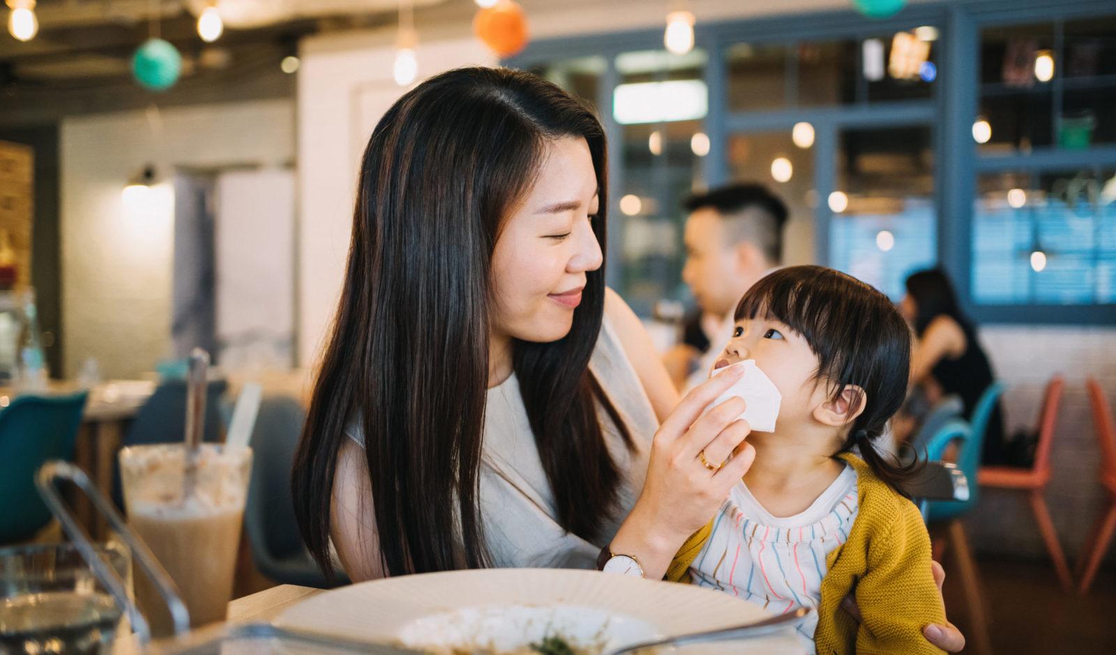 在餐馆里，年轻的母亲在饭后为女儿擦嘴